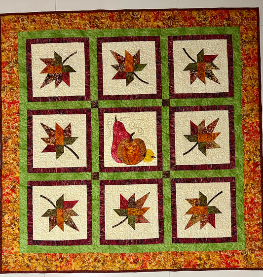 Handmade fall quilt with maple leaf and pumpkin design in autumn colors.