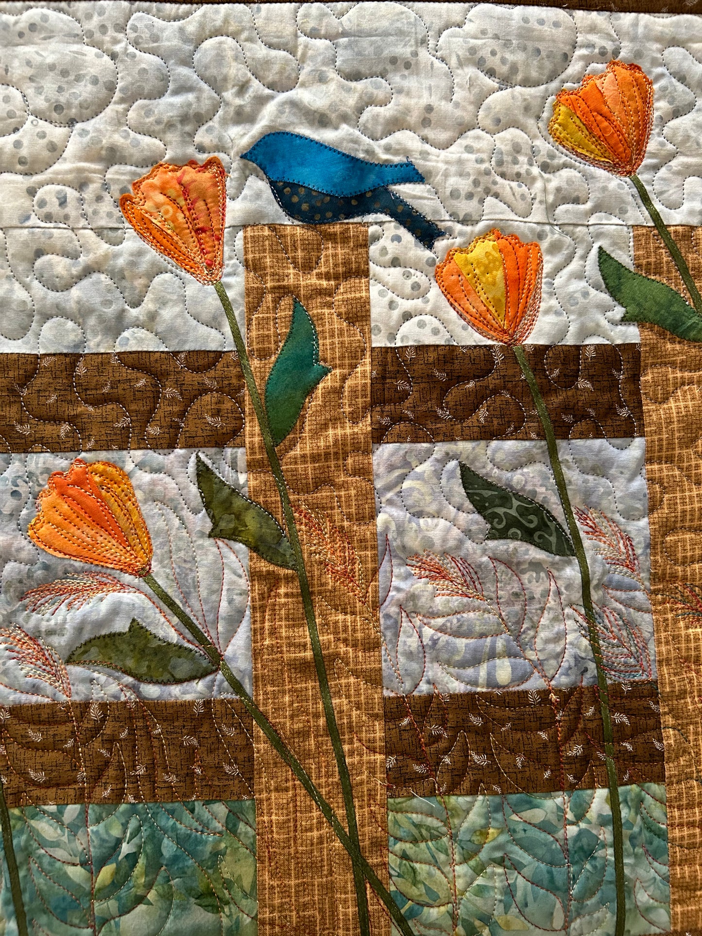 Close-up of fence flower motif and bird appliqué on quilted table runner