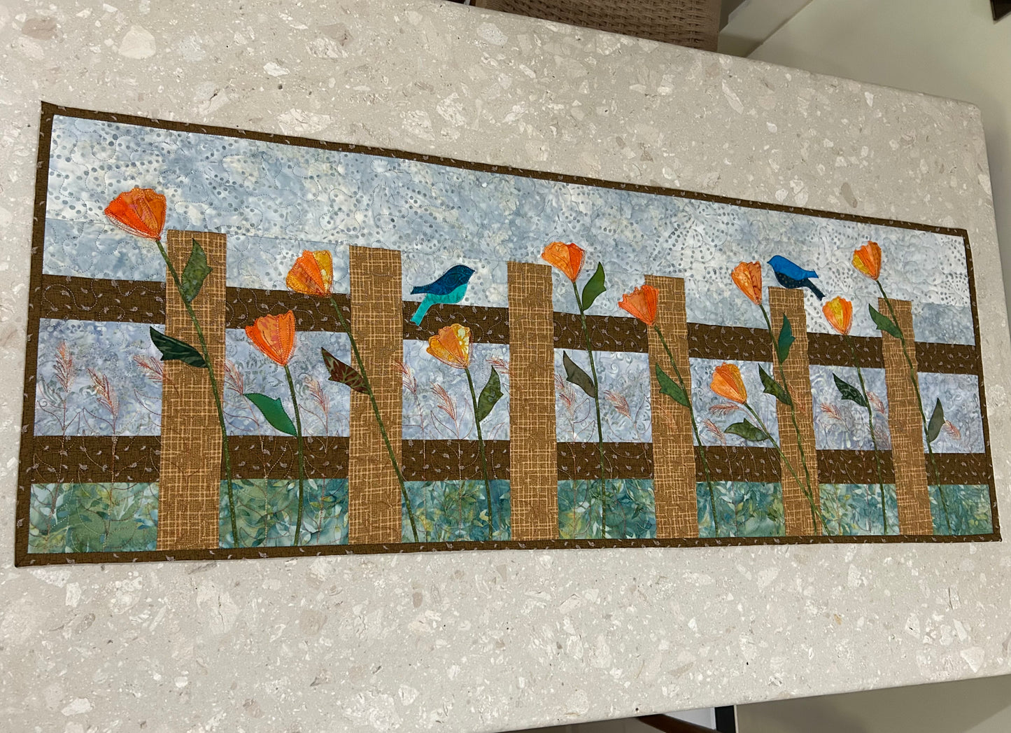 Handmade quilted table runner with fence and flower design on table