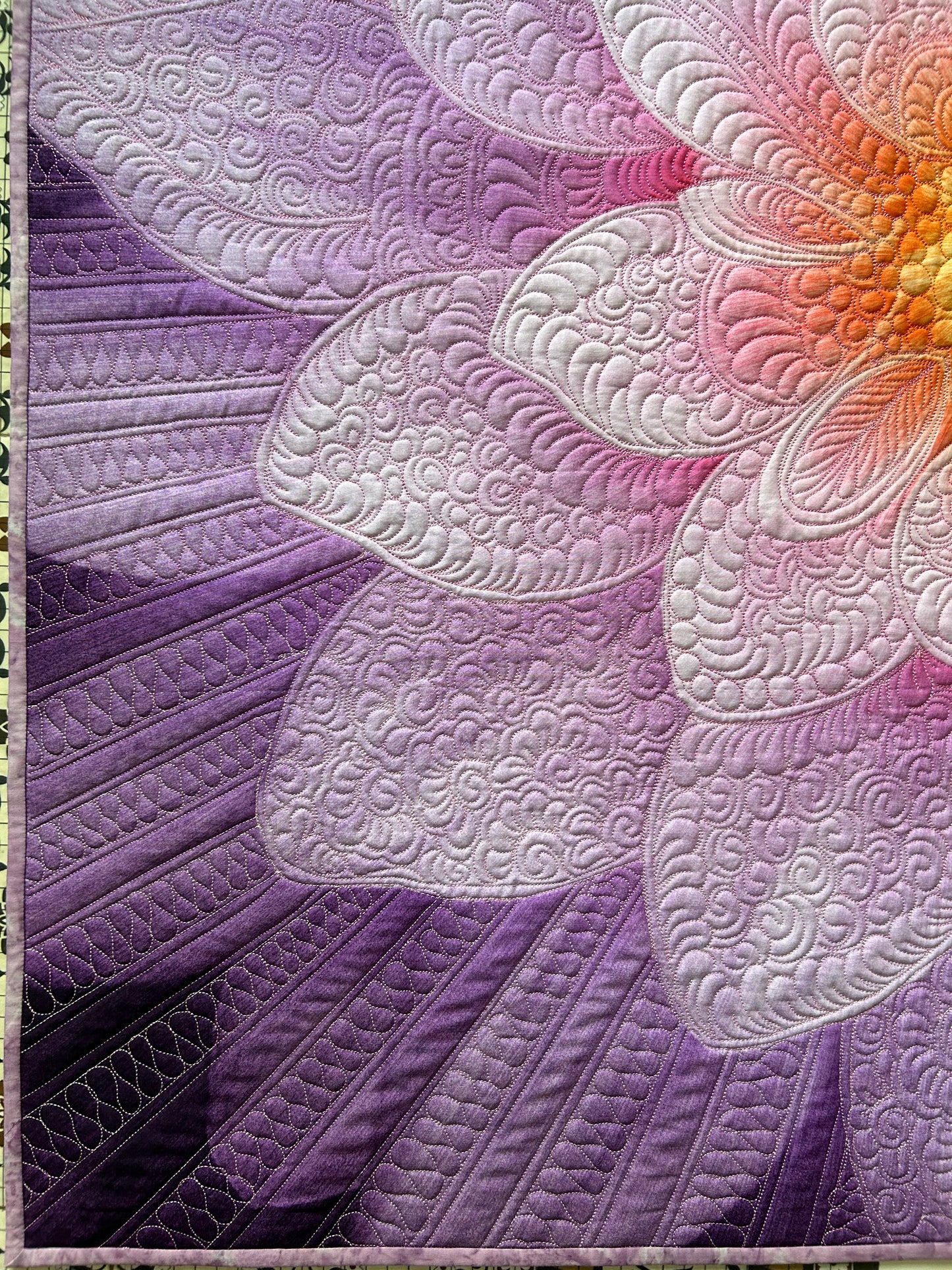 Close-up of detailed quilting on purple floral wall art.