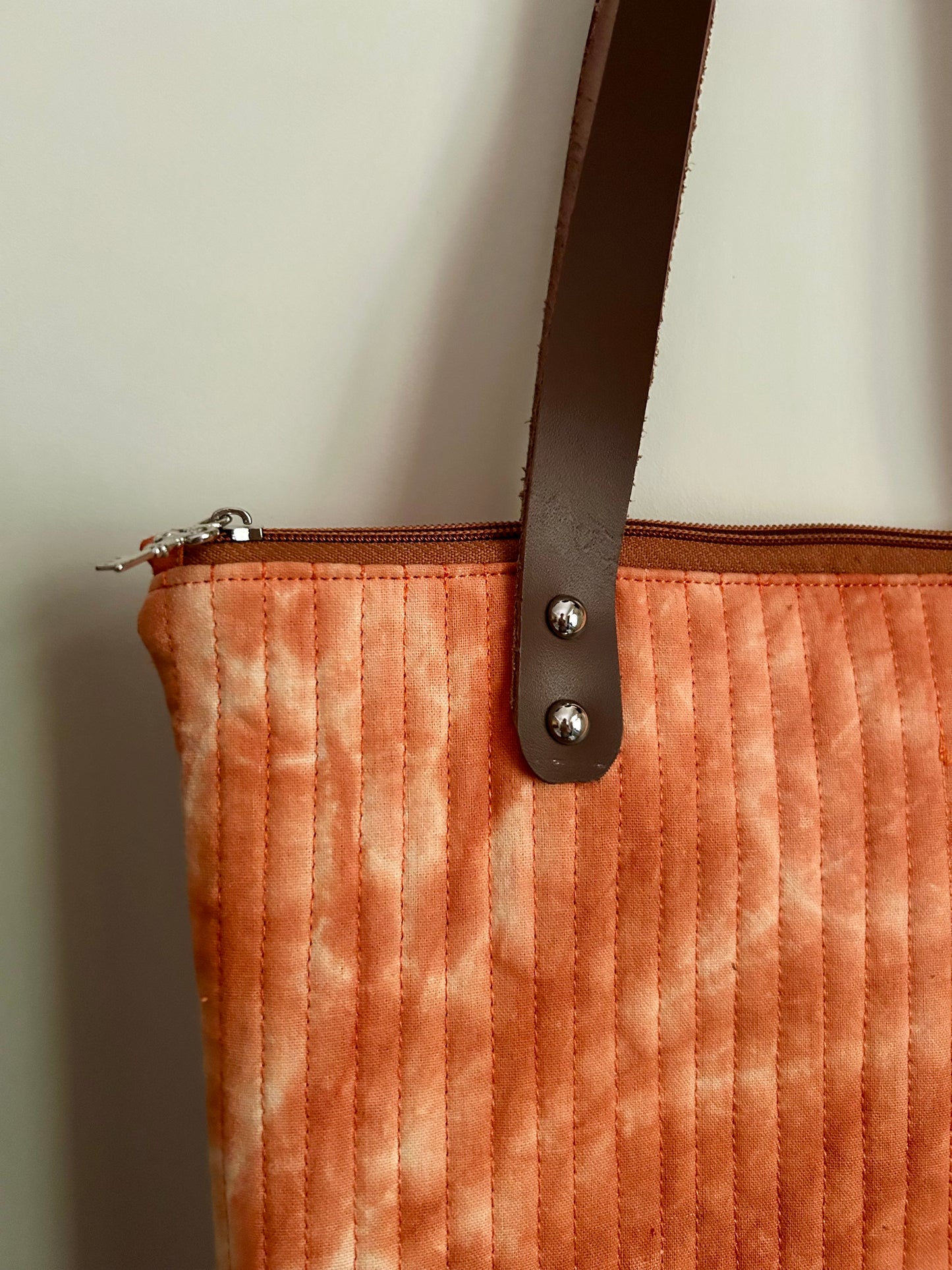 Details showing zipper pull and handle attachment on rust orange bag