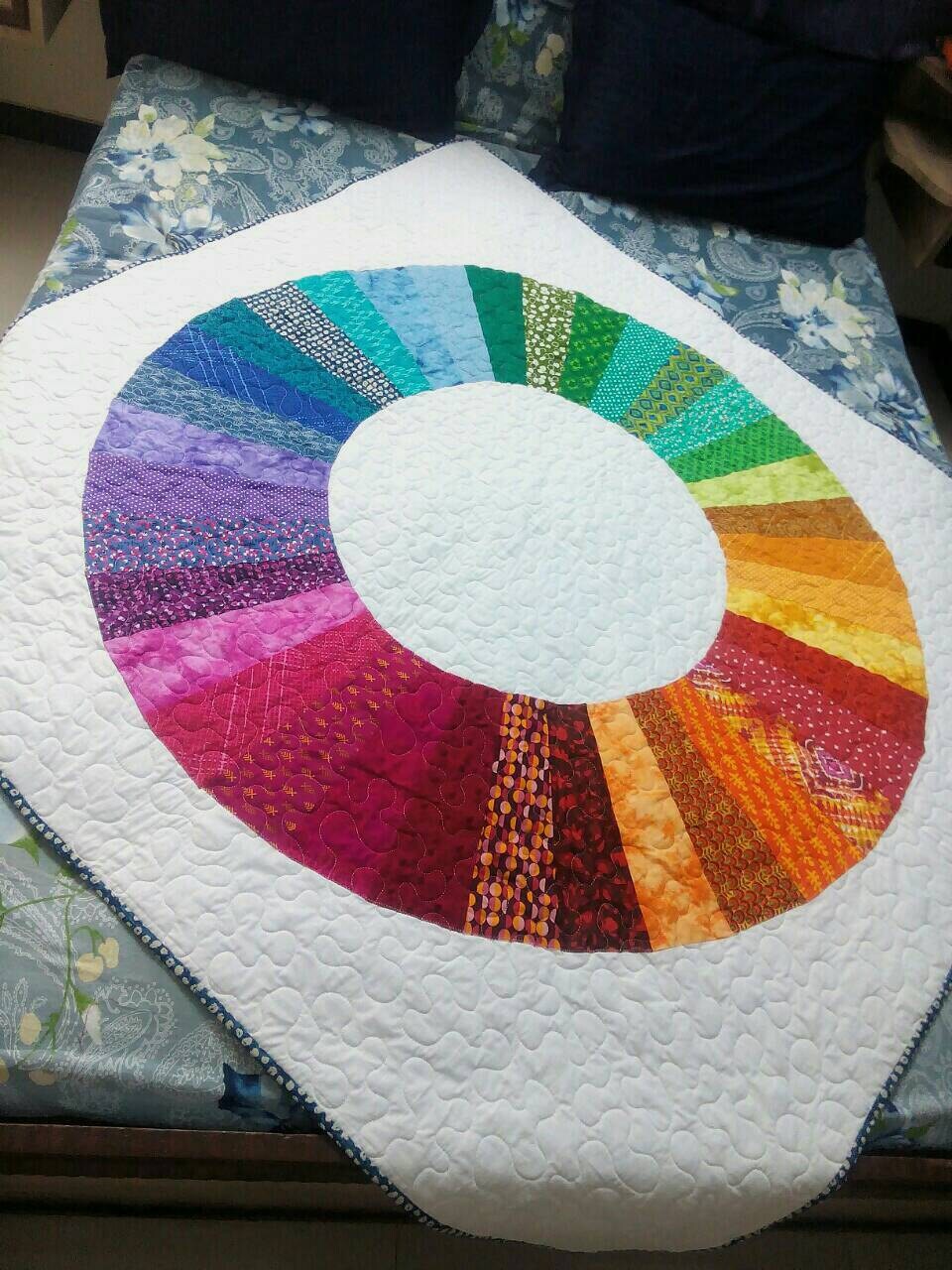 Handmade modern throw quilt with color wheel design on bed