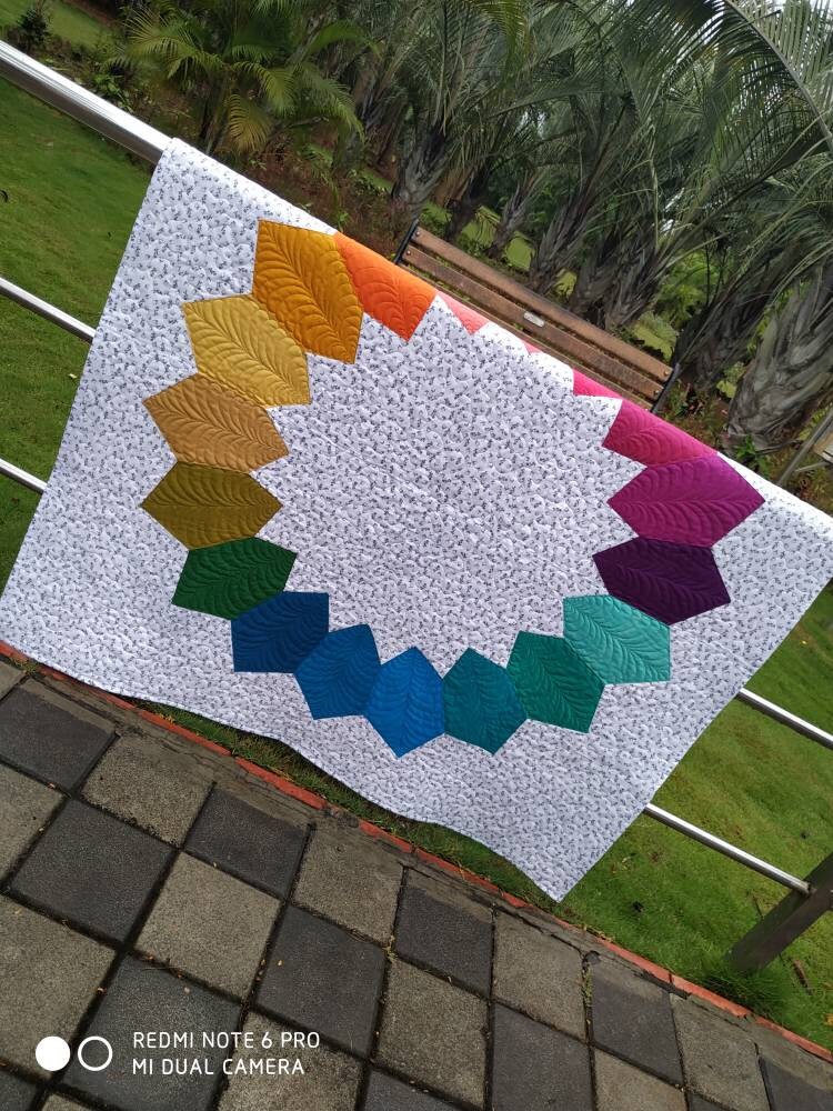Ombré throw quilt in natural light folded half on a bar in a garden