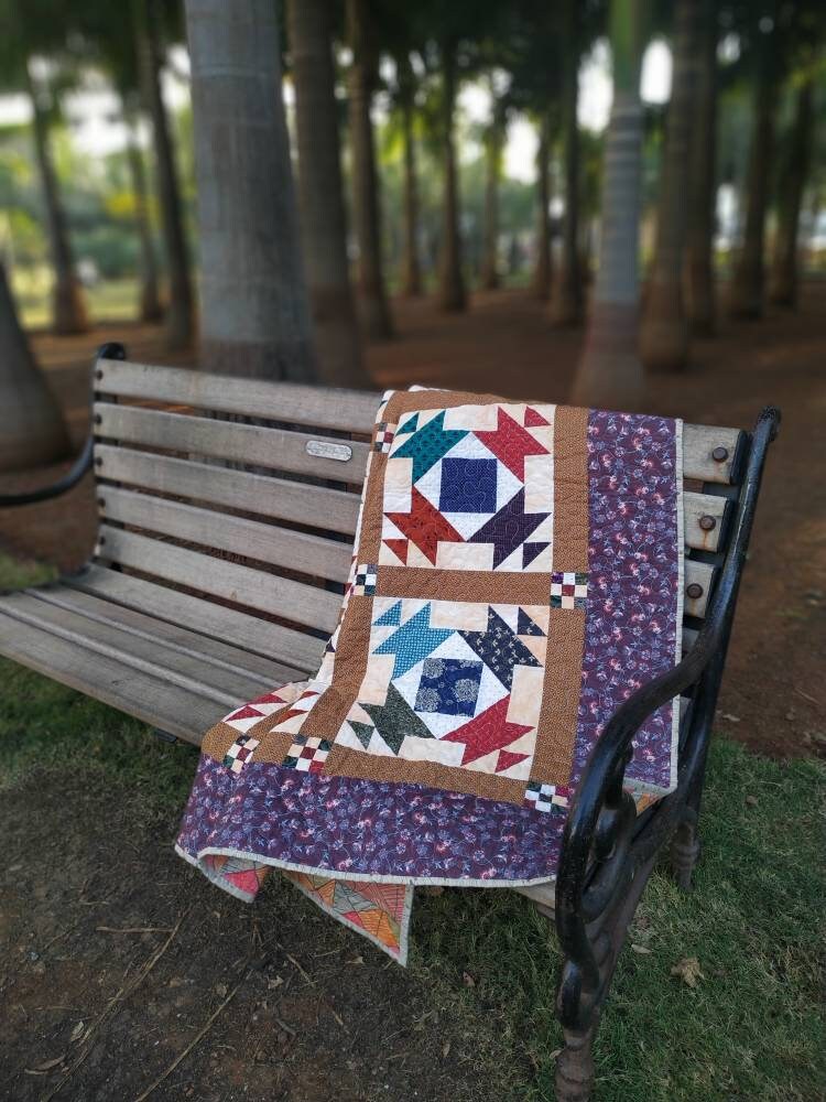 Country-style lap quilt draped on wooden bench 